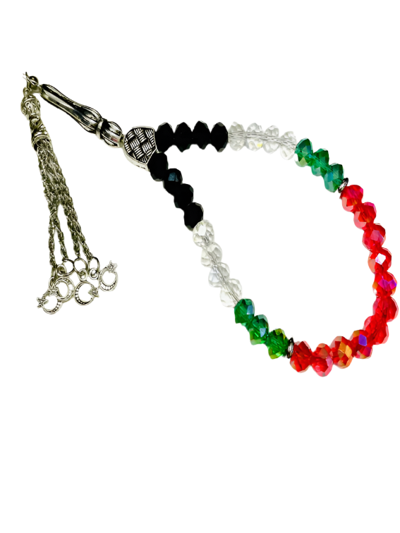 An elegant rosary featuring a design inspired by the colors of the Palestinian flag, where lustrous crystal beads in red, green, white, and black alternate, giving it a distinctive national character. metallic spacers are interspersed between the beads, enhancing their sparkle and allure. The rosary is crowned with dangling silver metallic tassels, consisting of delicate chains ending with metallic leaf-shaped ornaments, adding a touch of luxury and sophistication to the rosary as a whole.