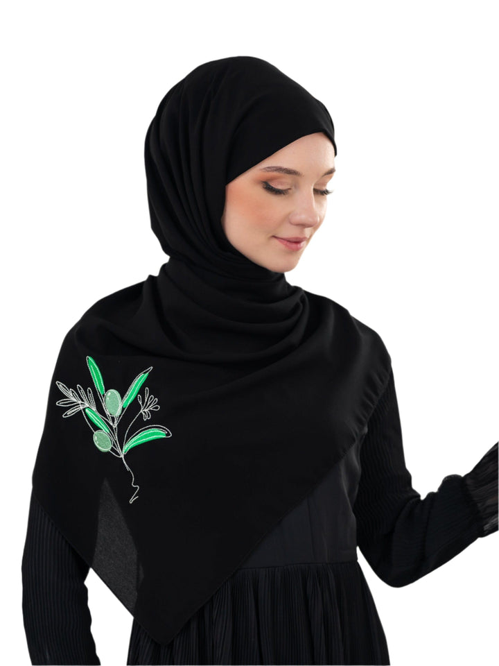 Discover expressive elegance with this luxurious black scarf, meticulously crafted from high-quality polyester that offers a soft touch and perfect drape. Measuring 70 x 180 cm, the scarf is versatile for various styling preferences. It is adorned with exquisite and detailed embroidery of a vibrant green olive branch, which is not merely an embellishment, but a profound symbol of peace, resilience, and a deep connection to the land and the rich Palestinian identity. Wear this scarf to express your refined t