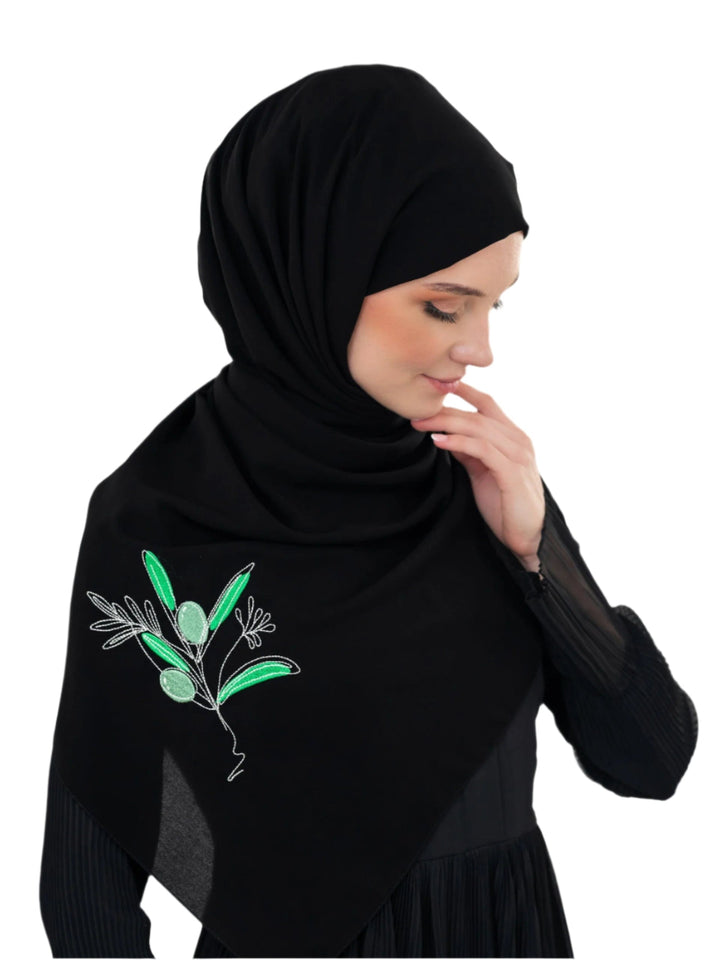Discover expressive elegance with this luxurious black scarf, meticulously crafted from high-quality polyester that offers a soft touch and perfect drape. Measuring 70 x 180 cm, the scarf is versatile for various styling preferences. It is adorned with exquisite and detailed embroidery of a vibrant green olive branch, which is not merely an embellishment, but a profound symbol of peace, resilience, and a deep connection to the land and the rich Palestinian identity. Wear this scarf to express your refined t