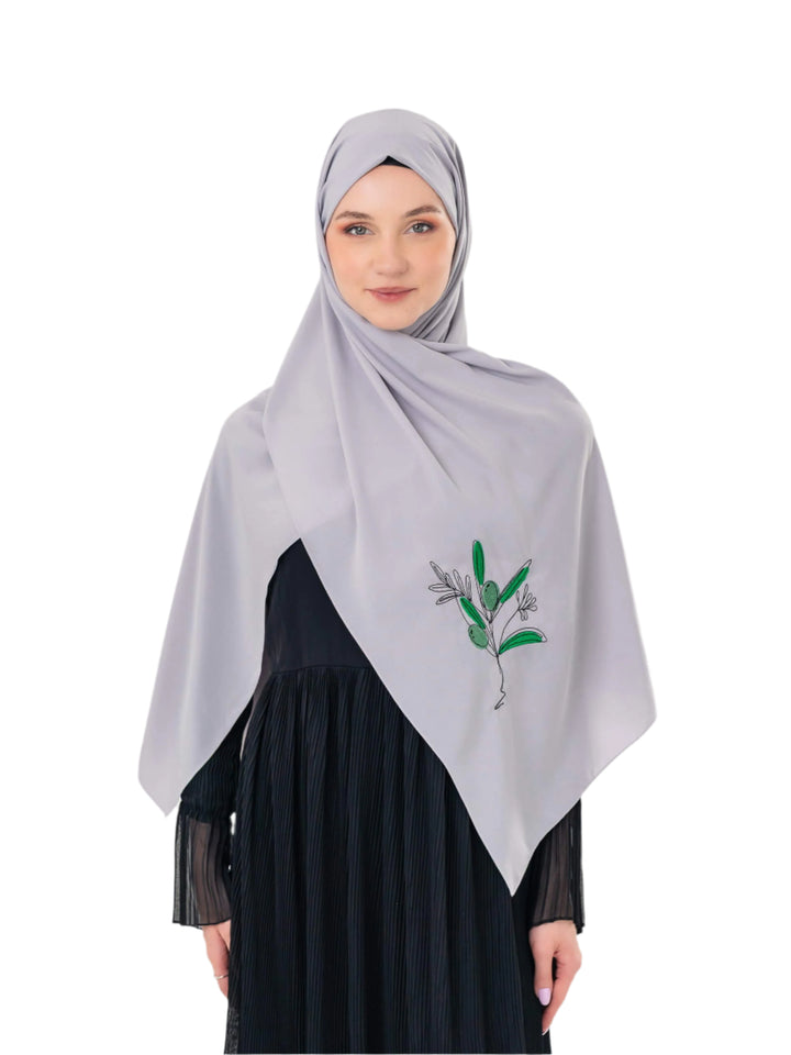 Woman wearing a light gray hijab with green embroidery on a white background