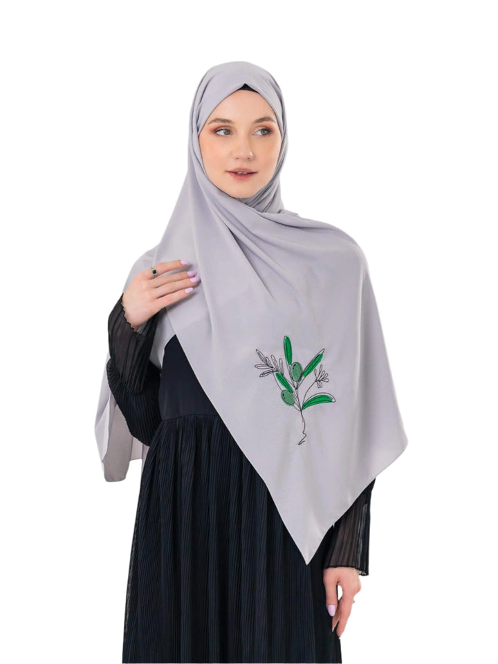 Woman wearing a light gray hijab with floral embroidery on a white background