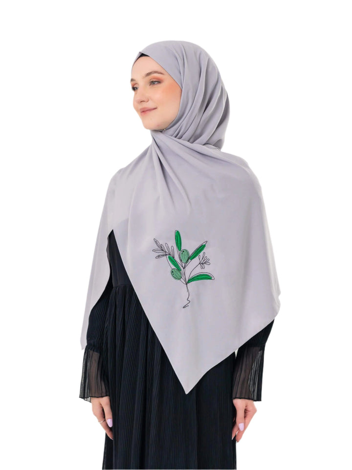 Woman wearing a light gray hijab with green leaf design on a white background