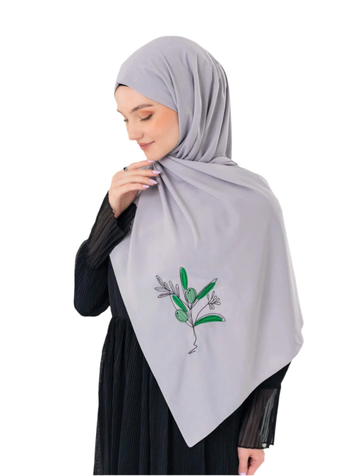 Woman wearing a light gray hijab with green leaf design on a white background