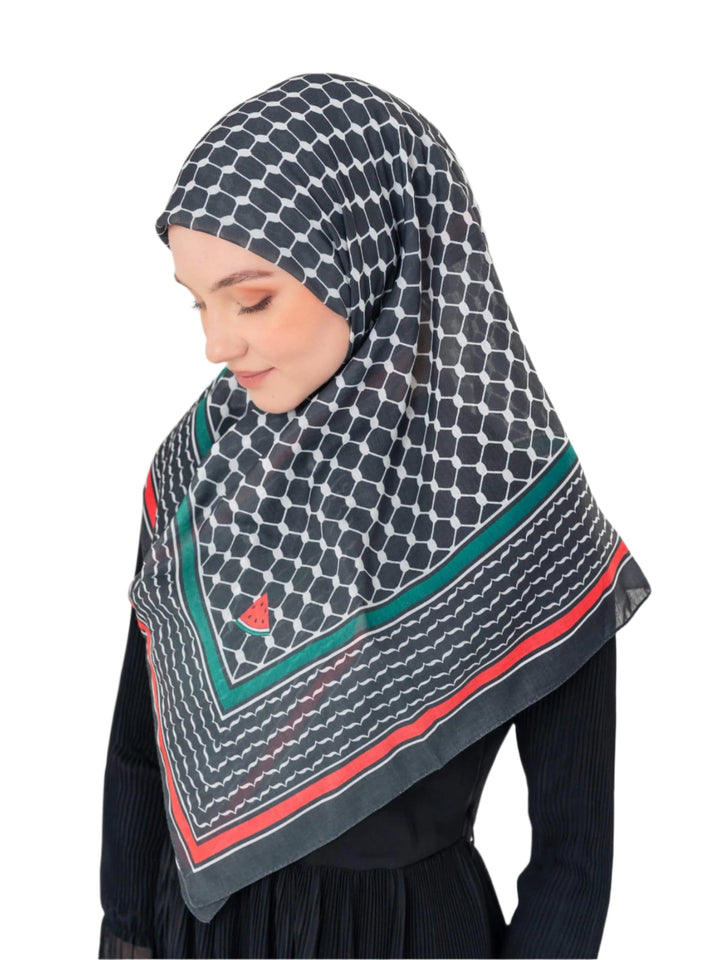 Woman wearing a patterned hijab with red and green accents on a plain background
