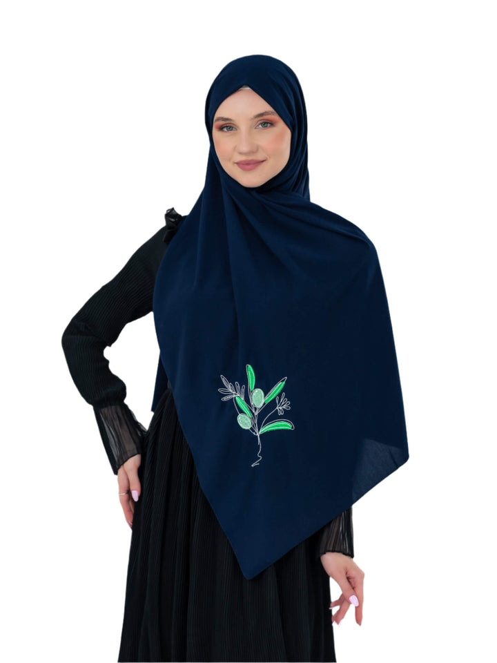 Woman wearing a navy hijab with green floral embroidery on a white background
