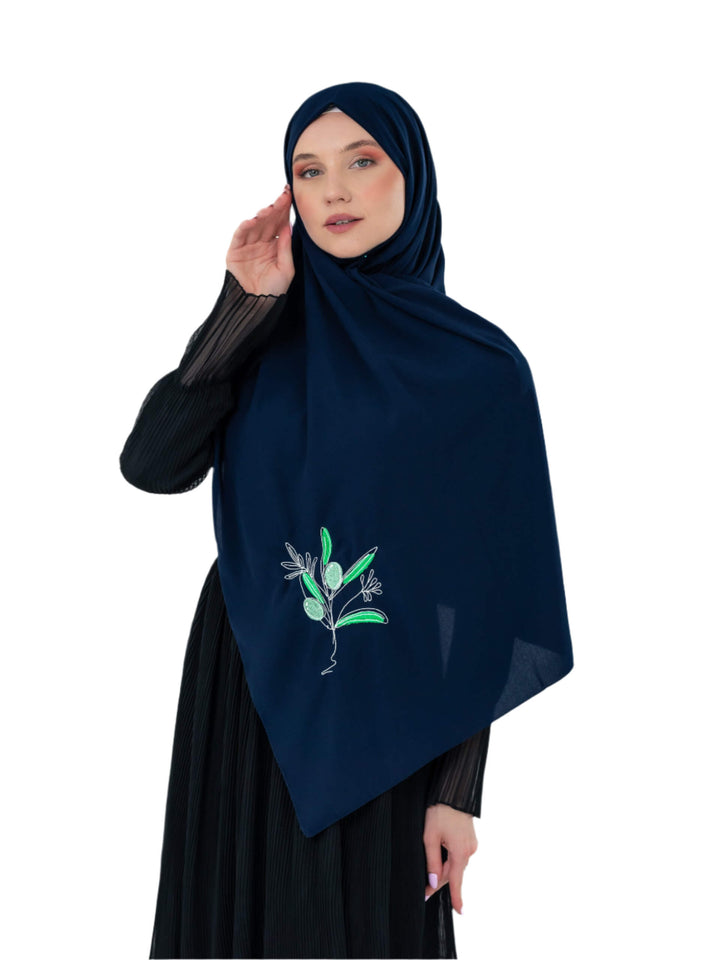 Woman wearing a navy hijab with green floral embroidery on a white background