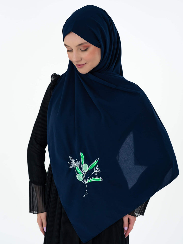 Woman wearing a navy blue hijab with floral embroidery on a white background